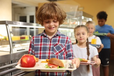 Photo of Little boy with tray of tasty food in school canteen, selective focus