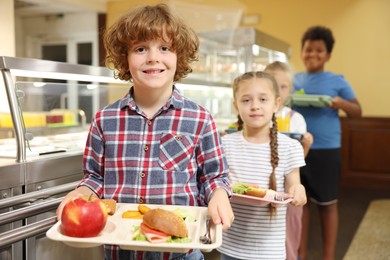 Photo of Little boy with tray of tasty food in school canteen, selective focus