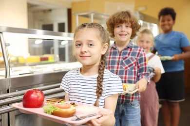 Photo of Little girl with tray of tasty food in school canteen, selective focus