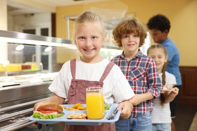 Photo of Little girl with tray of tasty food in school canteen, selective focus