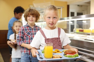 Photo of Little girl with tray of tasty food in school canteen, selective focus