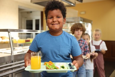 Photo of Little boy with tray of tasty food in school canteen, selective focus