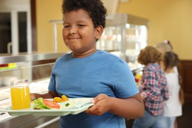 Photo of Little boy with tray of tasty food in school canteen, selective focus