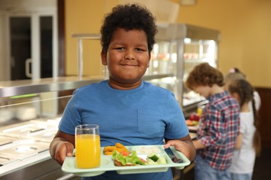 Photo of Little boy with tray of tasty food in school canteen, selective focus