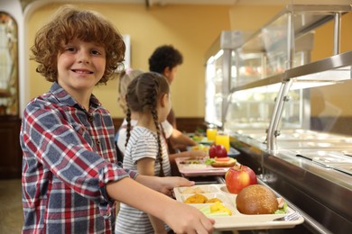 Photo of Little boy with tray of tasty food in school canteen, selective focus