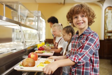 Photo of Little boy with tray of tasty food in school canteen, selective focus