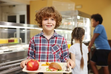 Photo of Little boy with tray of tasty food in school canteen, selective focus