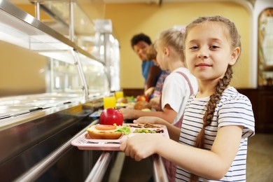Photo of Little girl with tray of tasty food in school canteen, selective focus