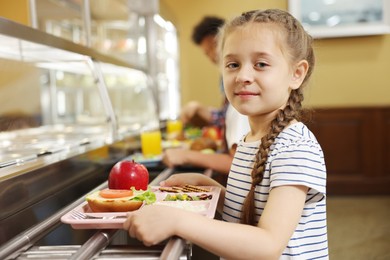 Photo of Little girl with tray of tasty food in school canteen, selective focus