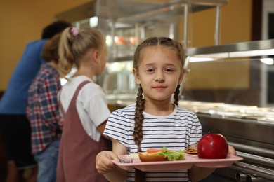 Photo of Little girl with tray of tasty food in school canteen, selective focus