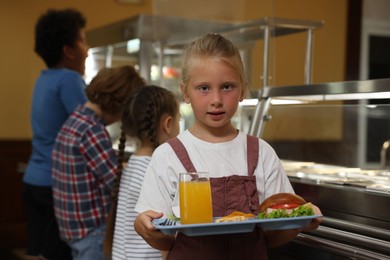 Photo of Little girl with tray of tasty food in school canteen, selective focus