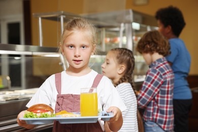 Photo of Little girl with tray of tasty food in school canteen, selective focus