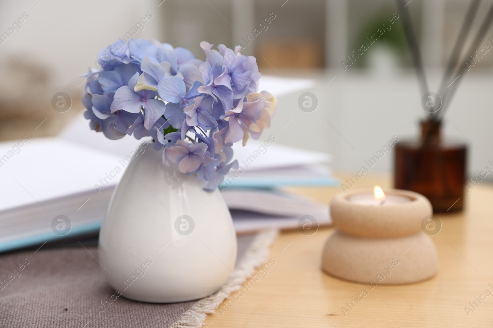 Spa composition with burning candle, reed air freshener, beautiful hydrangea flowers and book on table, selective focus Photo of Spa composition with burning candle, reed air freshener, beautiful hydrangea flowers and book on table, selective focus