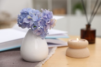 Photo of Spa composition with burning candle, reed air freshener, beautiful hydrangea flowers and book on table, selective focus