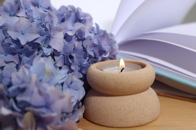 Photo of Spa composition with burning candle, beautiful hydrangea flowers and book on wooden table, closeup