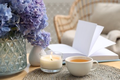 Photo of Spa composition with burning candle, beautiful hydrangea flowers, tea and book on table, closeup