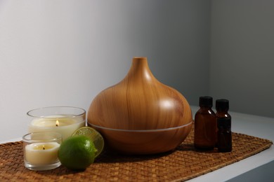 Photo of Spa composition with aroma oil diffuser, burning candles and cosmetic products on table indoors