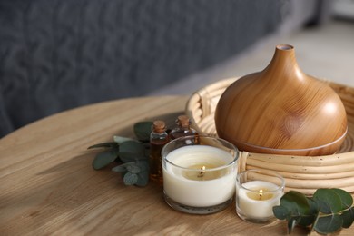 Photo of Spa composition with aroma oil diffuser and burning candles on wooden table indoors, closeup