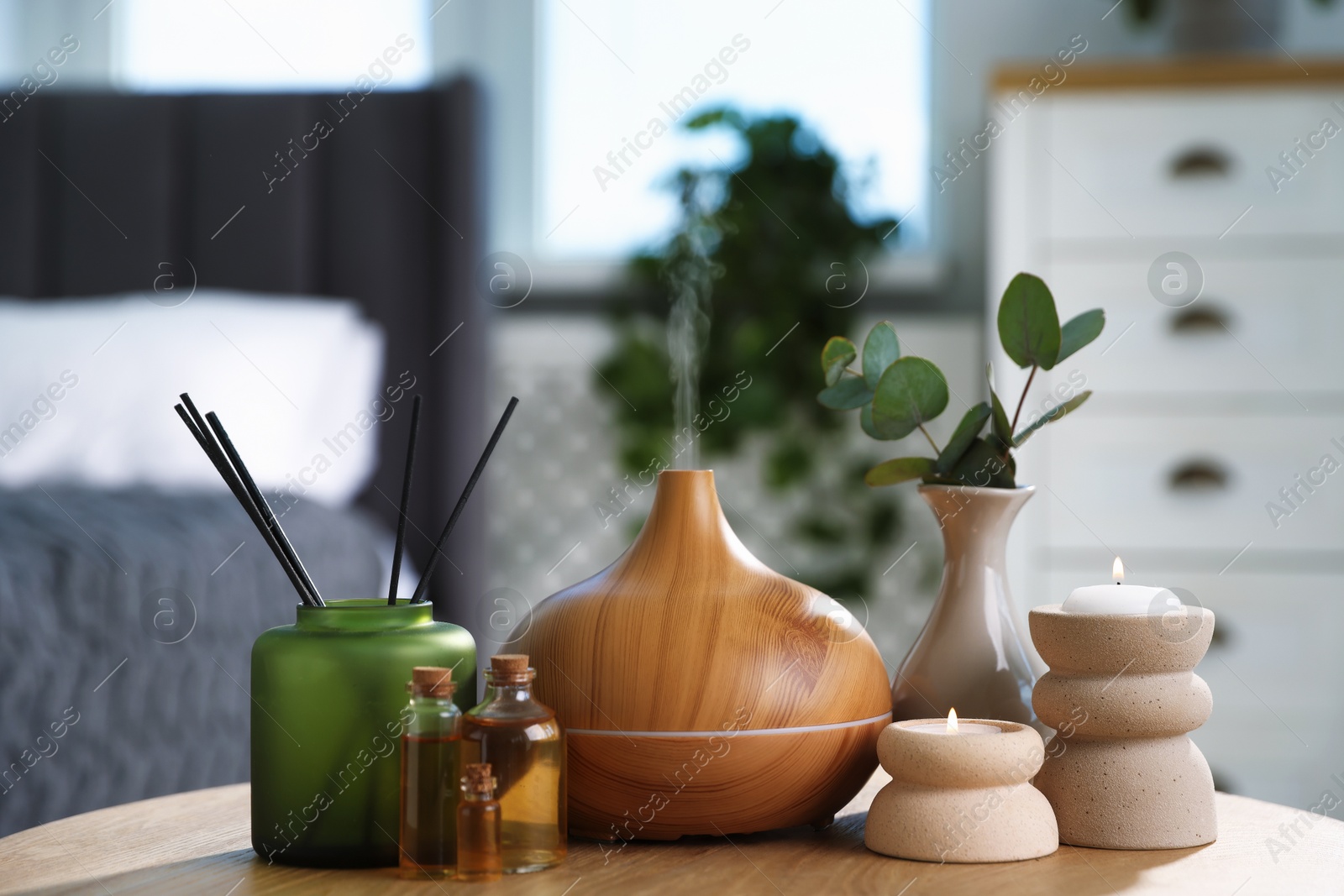 Spa composition with aroma oil diffuser, reed air freshener and burning candles on wooden table indoors Photo of Spa composition with aroma oil diffuser, reed air freshener and burning candles on wooden table indoors