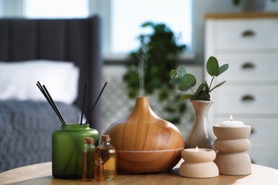 Photo of Spa composition with aroma oil diffuser, reed air freshener and burning candles on wooden table indoors