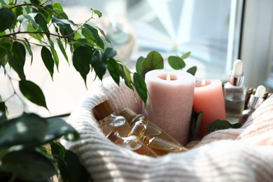 Photo of Spa composition. Burning candles and cosmetic products in basket with blanket indoors, closeup