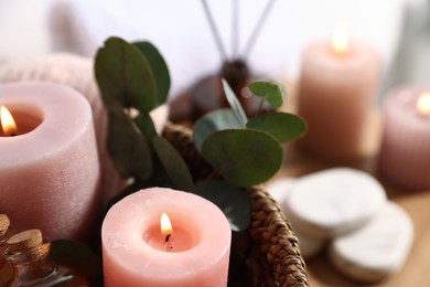 Photo of Spa composition. Burning candles, cosmetic products and eucalyptus branches in basket on table, closeup