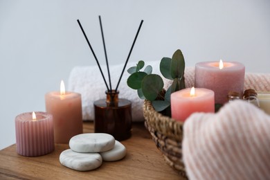 Photo of Spa composition with burning candles and reed air freshener on wooden table indoors, closeup