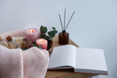Photo of Spa composition with burning candles and reed air freshener on wooden table indoors, closeup
