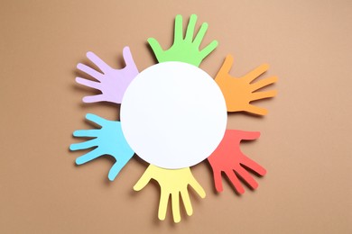 Photo of Tolerance concept. Colorful paper hands and empty card on brown background, top view. Space for text