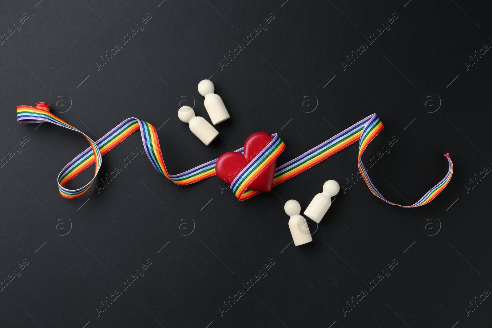 Tolerance concept. Human figures, heart and colorful ribbon on black background, flat lay Photo of Tolerance concept. Human figures, heart and colorful ribbon on black background, flat lay