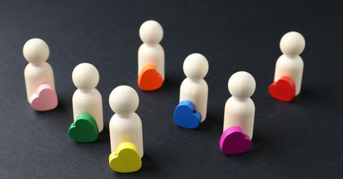 Photo of Tolerance concept. Human figures and colorful hearts on black background, closeup