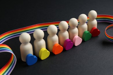 Photo of Tolerance concept. Human figures, colorful hearts and ribbon on black background, closeup