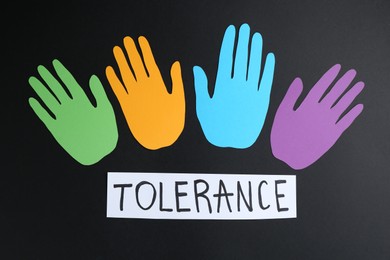 Photo of Card with word Tolerance and colorful paper hands on black background, flat lay