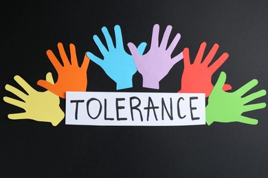 Photo of Card with word Tolerance and colorful paper hands on black background, flat lay