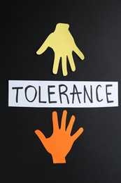 Photo of Card with word Tolerance and colorful paper hands on black background, flat lay