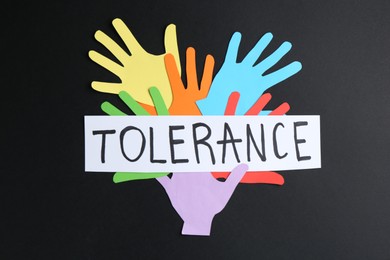 Photo of Card with word Tolerance and colorful paper hands on black background, flat lay