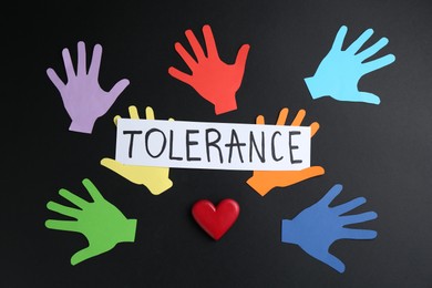 Photo of Card with word Tolerance and colorful paper hands on black background, flat lay