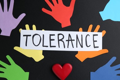Photo of Card with word Tolerance and colorful paper hands on black background, flat lay