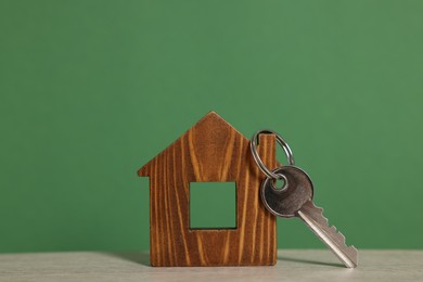 Photo of Home security. House model with key on wooden table against green background, closeup