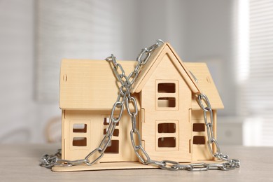 Photo of Home security. House model with chain on wooden table indoors, closeup