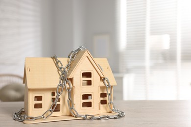 Photo of Home security. House model with chain on wooden table indoors, space for text