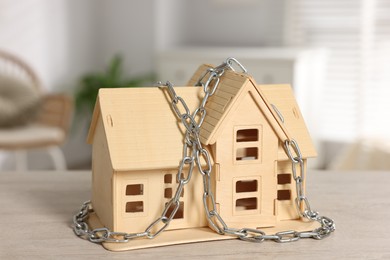 Photo of Home security. House model with chain on wooden table indoors, closeup
