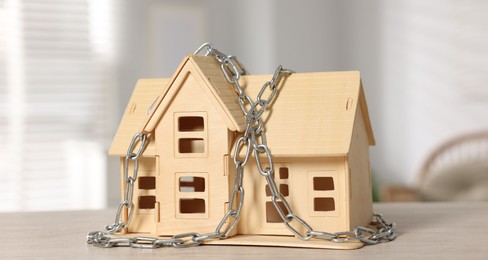 Photo of Home security. House model with chain on wooden table indoors, closeup