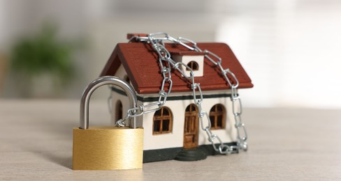 Photo of Home security. House model with chain and padlock on wooden table, closeup