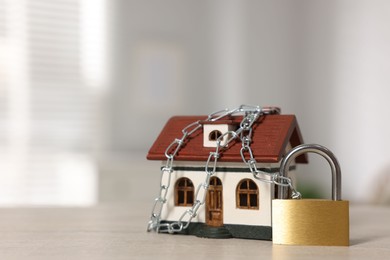 Photo of Home security. House model with chain and padlock on wooden table, closeup. Space for text