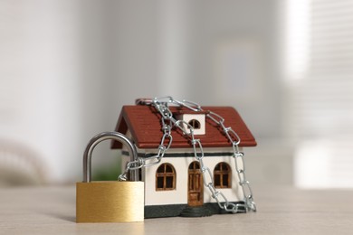 Photo of Home security. House model with chain and padlock on wooden table, closeup