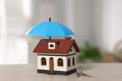 Photo of Home security. House model with small umbrella and keys on wooden table indoors, closeup