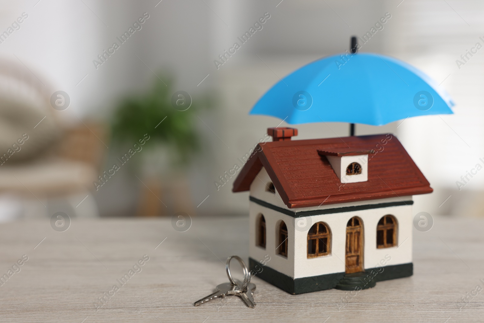Photo of Home security. House model with small umbrella and keys on wooden table indoors, closeup. Space for text