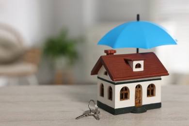 Photo of Home security. House model with small umbrella and keys on wooden table indoors, closeup. Space for text