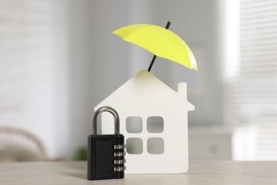 Photo of Home security. House model with small umbrella and padlock on wooden table indoors, closeup